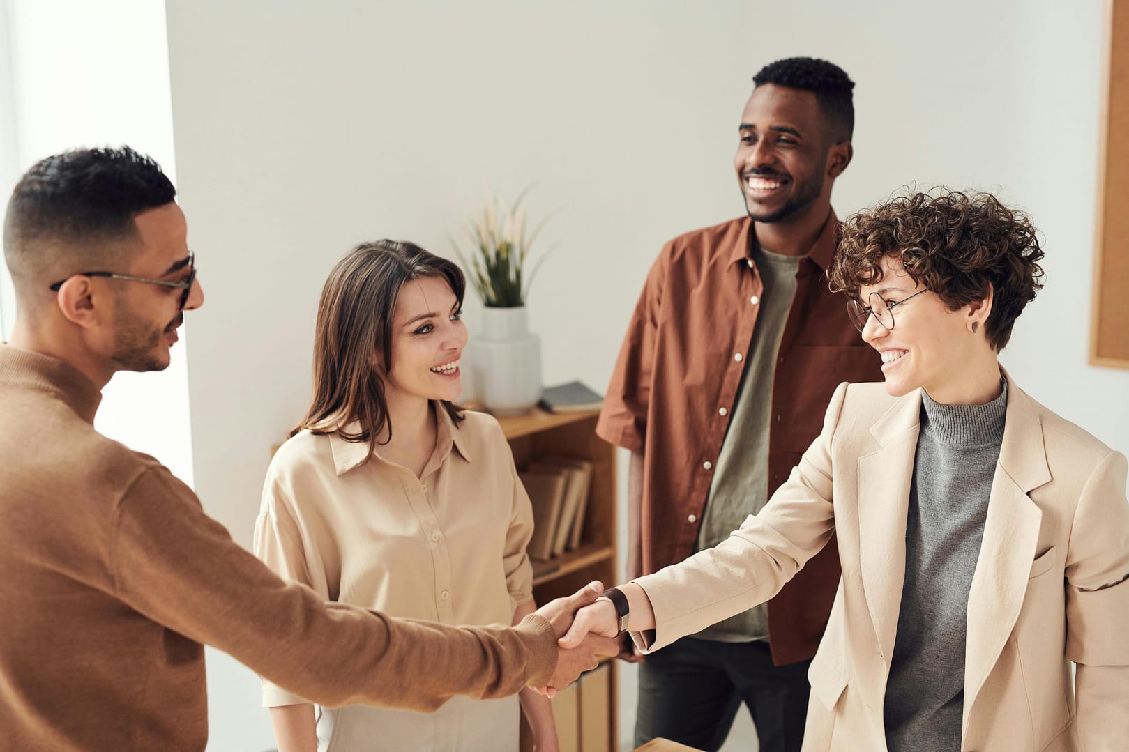 pexels photo 3184416 3184416 Four colleagues smiling and shaking hands in a bright office setting.